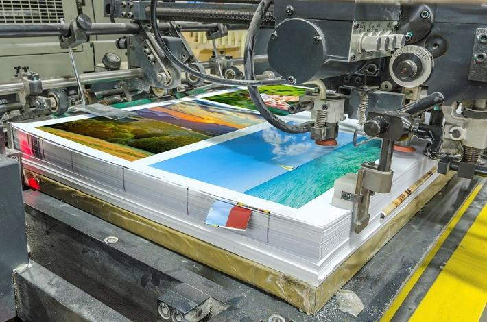 Industrial printing press producing stacked full-color printed pages on a production line.