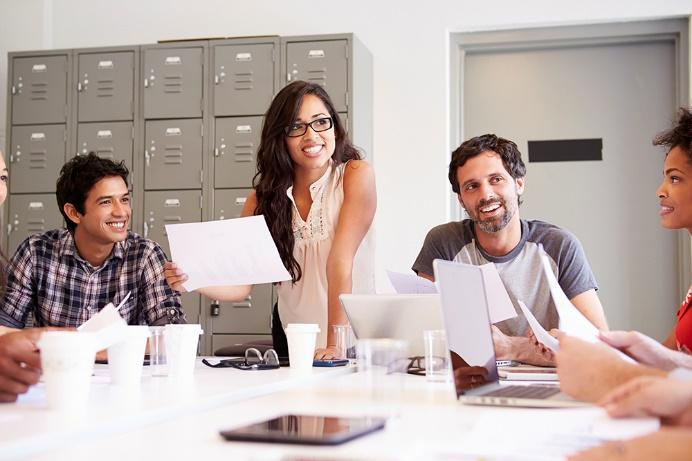 Group of colleagues in a meeting room collaborate around a table, reviewing papers and discussing ideas.