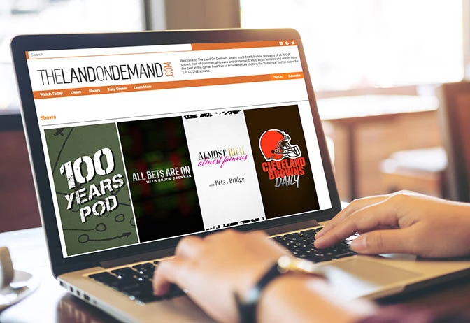 Person using a laptop to browse a website featuring podcasts and audio show listings.